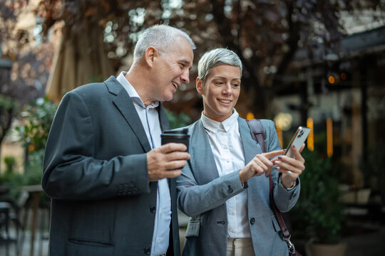 Business people collaborating on smartphone smiling outdoors - Powered by Adobe