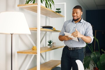 Black male entrepreneur standing in office near bookshelf and holding documents