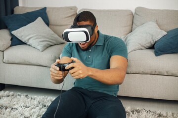 Black guy with virtual reality glasses sitting on a carpet in living room