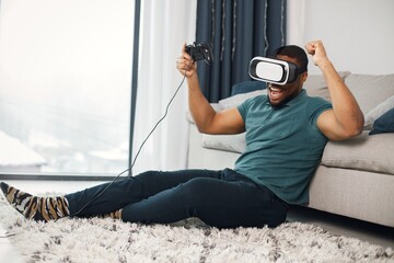 Black guy with virtual reality glasses sitting on a carpet in living room