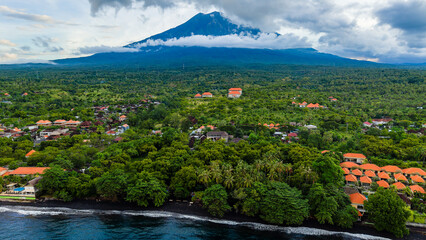 Aerial drone view of Tulamben village and black sand beach with Mount Agung volcano
