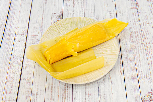 Sweet and savory humitas are displayed in their opened corn husks, revealing the corn dough with cheese and caramelized onions.