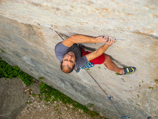 CLOSE UP, TOP DOWN: Male climber battles up a steep limestone wall, gripping a thin crack in a technical crux. focus, precise movement and the intensity of lead climbing on a demanding outdoor route.