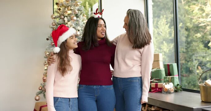 Festive tree inspiring Diverse three-gen family wearing Santa hat, antler headband laughing at home