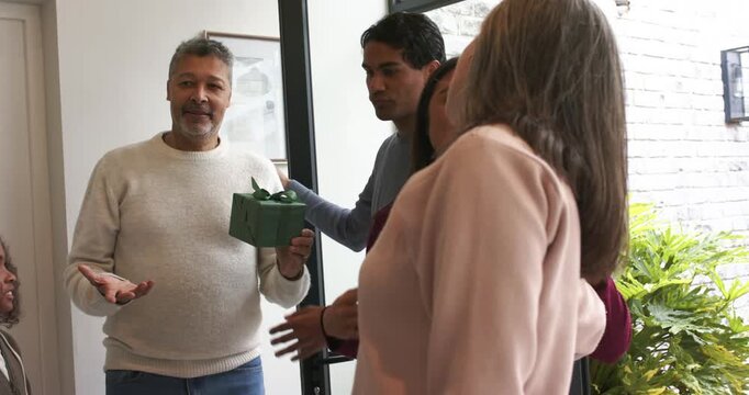 Entering foyer child greeting diverse family while senior man offering wrapped green gift box