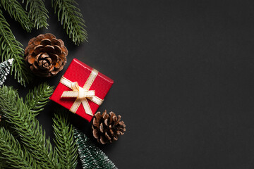 Christmas flat lay with red gift box, pinecones, fir branches, berries, and mini trees on black background. Perfect for elegant holiday greeting cards, festive promotions, and seasonal design.