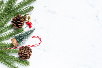 Flat lay of Christmas decorations with fir branches, pine cone, gift boxes, and candy canes on white marble background. Perfect for holiday greeting templates, winter design, and festive ads.