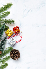 Flat lay of Christmas decorations with fir branches, pine cone, gift boxes, and candy canes on white marble background. Perfect for holiday greeting templates, winter design, and festive ads.