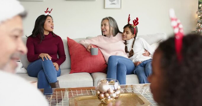 After silent pause, diverse family sitting on sofa sharing holiday chat while holding ceramic mug