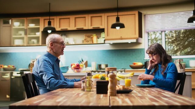 Mature wife appears overwhelmed and uninterested with silent irritation while her husband talks, creating candid marriage moment in retirement. Uninterested detached woman, melancholy. Camera A.
