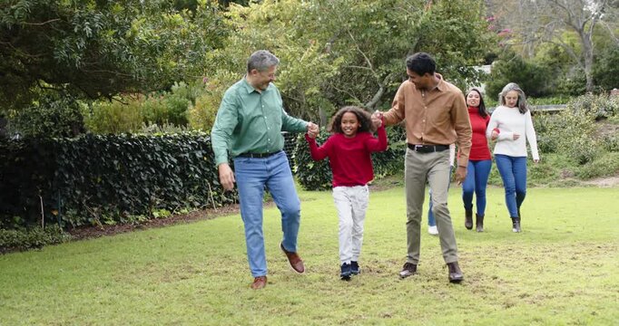 Upon granddad and dad swinging child's hands, extended family strolling on lawn pointing ahead