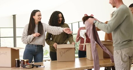 Diverse volunteers finding donation boxes and jars sorting items packing them taping boxes at table