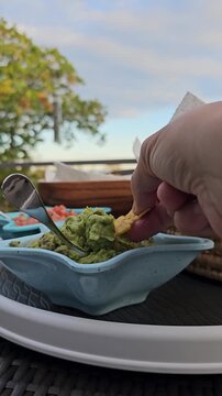 Hand dipping chip into guacamole dip vertical video