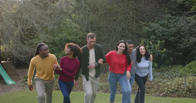 Diverse friends linking arms and climbing grassy park lawn for support under soft sunlight