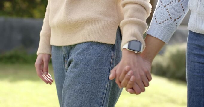 After pausing couple strolling forward with interlocked hands tracking smartwatch past stone wall