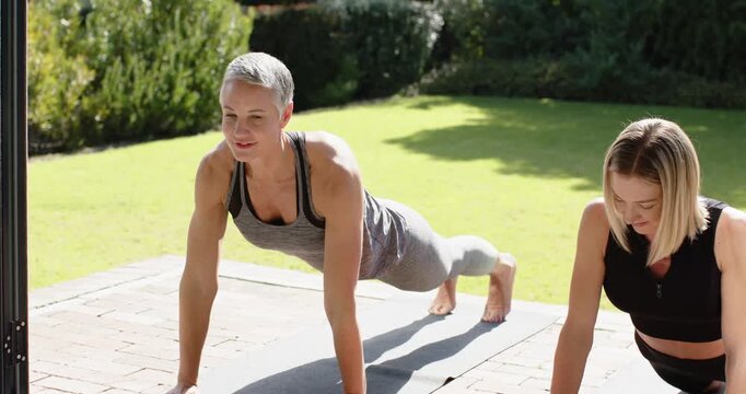 Female friends sliding into plank triggered by grey-haired friend for core strength on patio mats
