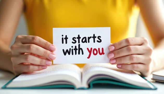Woman holds card with text starts with over open book. Positive message of self responsibility, personal growth. Focus on empowerment, motivation for life change. Decision making for future goals.