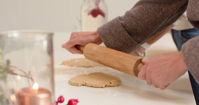 Two women are gripping rolling pin to flatten dough for cookie baking and are sharing laughter