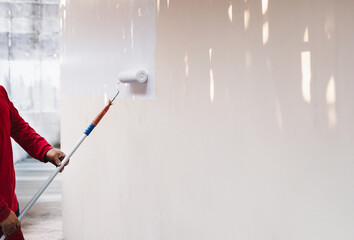 Painter painting an old wall with a paint roller in white color.