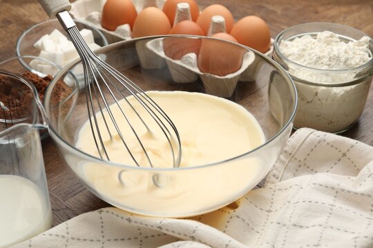 Different ingredients for dough and whisk on wooden table, closeup