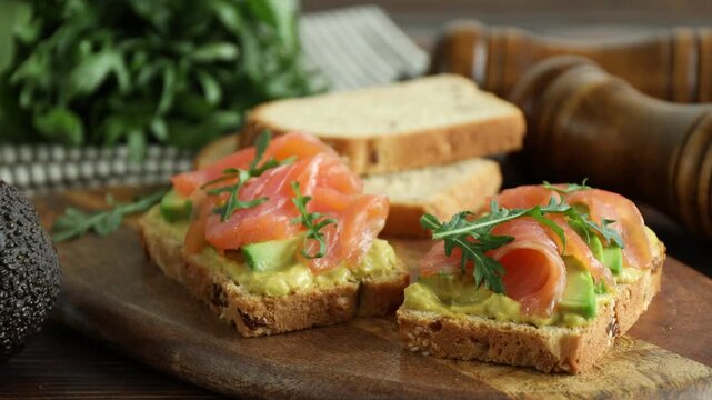 Tasty bruschettas with salmon, arugula and avocado on wooden table, closeup. Camera moving right