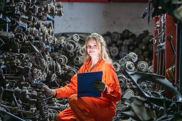 Female worker smiling in auto parts warehouse mechanic car parts industry Recycling repair of automotive industry. Worker orange jumpsuit smiling technician inspection secondhand recycle parts