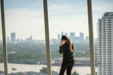 Obraz premium architect woman in suit thinking planning thoughtful inspection on empty office interior near glass window. office interior standing thinking planning thoughtful with blueprint on skyscraper floor