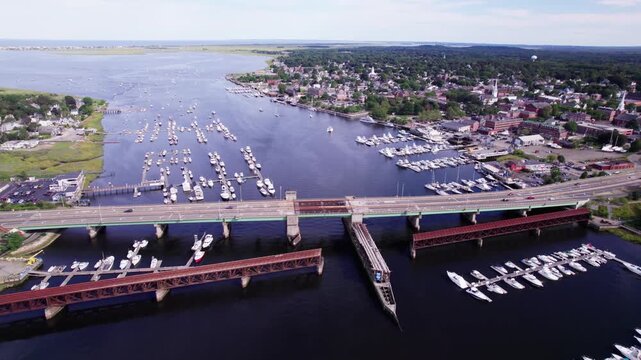 Newburyport, Massachusetts along the Merrimack river. The Gillis bridge with traffic is seen, with boats docked and the mouth of the river in the distance.