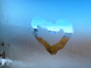 Heart painted on a foggy window. Outside the window is the road.
