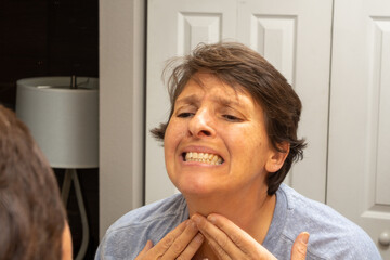 A woman in her early fifties looks in the mirror, concerned with her appearance. Beauty and aging concept