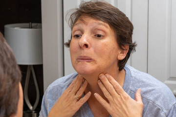 A woman in her early fifties looks in the mirror, concerned with her appearance. Beauty and aging concept