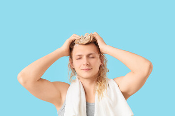 Fototapeta premium Young blonde man washing hair on blue background