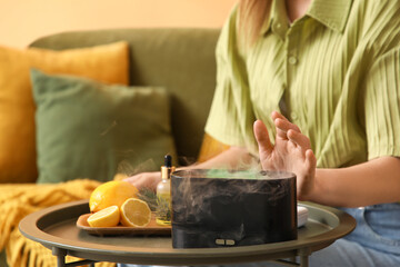 Woman with aroma diffuser and lemons on table at home, closeup