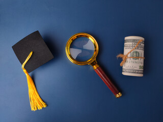 Miniature graduation cap, a magnifying glass, and a roll of US currency