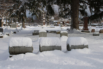 Three gray headstones covered in snow with others in the background at a small suburban Chicago cemetery