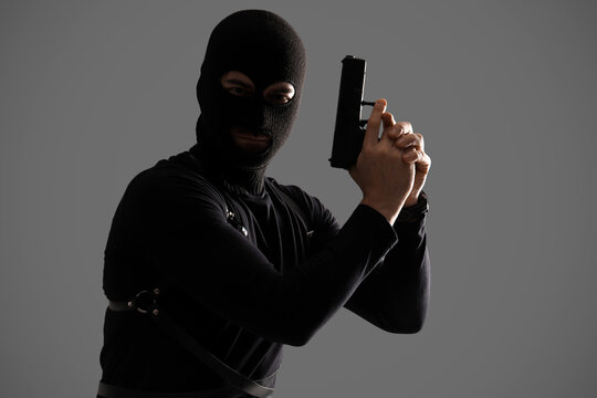 Male robber in balaclava with gun on grey background