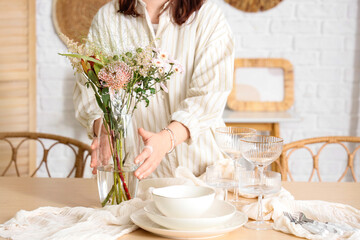 Young woman serving table with beautiful flowers in dining room