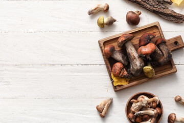 Board and bowl with fresh mushrooms on white wooden background