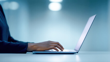 Side view hand typing on laptop modern office blue light minimal desk professional focus closeup detail workspace calm technology workflow evening work sleek device