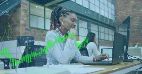 Woman typing, pausing and scrolling on laptop in open-plan office, reviewing financial chart