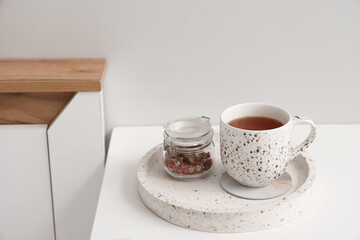 Coaster with cup of tea and dry hibiscus flowers on table in bedroom