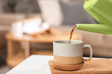 Pouring of coffee into cup with coaster on table in room, closeup