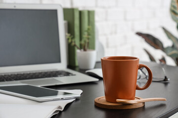 Cup of coffee with wooden coaster and spoon on desk in office, closeup