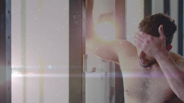 Camera pulling back shirtless man rubbing forehead, facing lens, modeling with animated lens flare