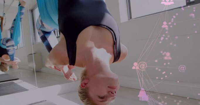 Woman holding inverted pose in yoga, hammock settling showing blue silk, pink overlay beside her