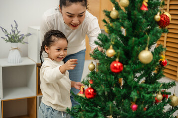 mother and toddler girl decorating Christmas tree at home
