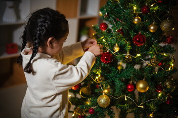 toddler girl decorating Christmas tree in home at night