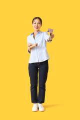 Young Asian woman with driving license and toy car on yellow background