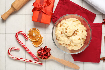 Bowl of dough for Panettone with ingredients and Christmas decor on white tile background