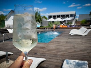 A glass of white cold wine with ice on the background of the pool, relaxation on a hot summer day